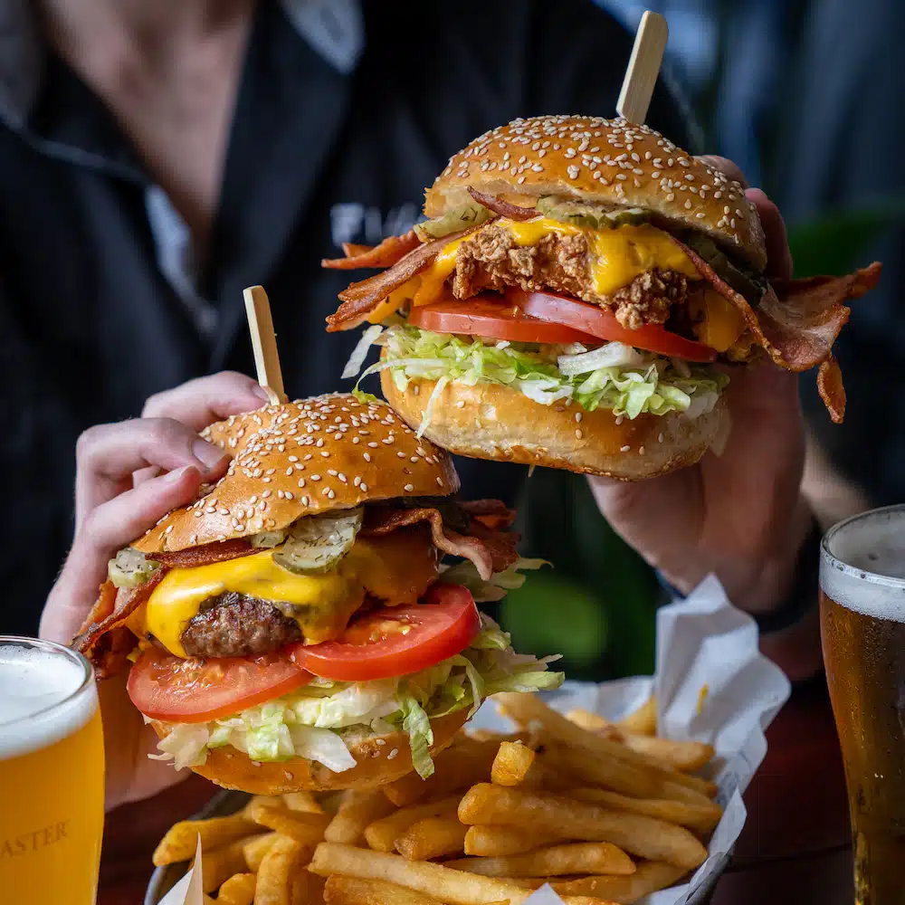 Two burgers being held up over a plate of chips